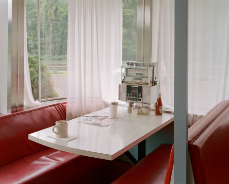 Tema Stauffer  Diner, Elizaville, New York, 2017, 2017  Archival Pigment Print  30h x 36w in 76.20h x 91.44w cm  Edition of 8  TS_023, Color photograph of a set table inside a roadside diner, red booths, tabletop jukebox, white sheet curtains