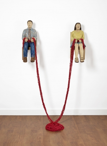 Sachiko Akiyama  Gathering, 2019  Wood, Paint,String  Dimensions Variable. a sculpture of two figures mounted to a wall with a length of red cord connecting them together and to the floor below.